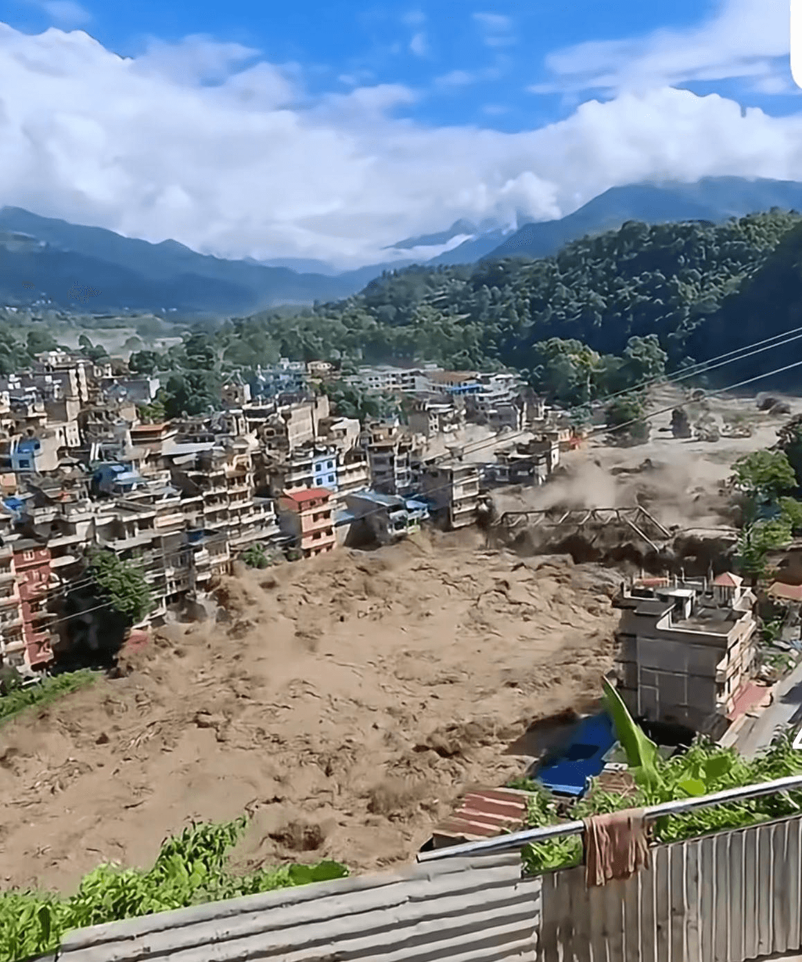 Muddy floodwaters surge through a riverside town in Nepal, damaging a bridge and buildings